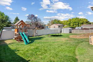 View of yard with a playground, a trampoline, and a storage unit