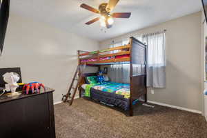 Carpeted bedroom with ceiling fan and a textured ceiling