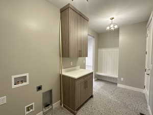 Clothes washing area with electric dryer hookup, hookup for a washing machine, cabinets, and an inviting chandelier