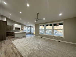 Unfurnished living room with ceiling fan with notable chandelier, light hardwood / wood-style floors, and lofted ceiling