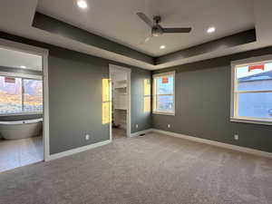 Unfurnished bedroom with ceiling fan, a raised ceiling, a spacious closet, and light carpet