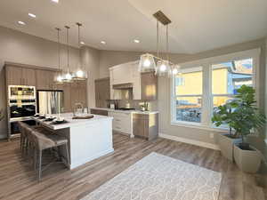 Kitchen with backsplash, a center island with sink, white cabinets, light hardwood / wood-style floors, and stainless steel appliances