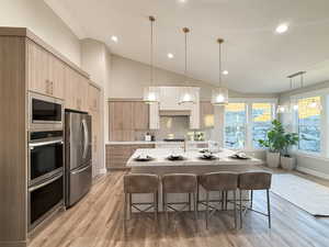 Kitchen with light brown cabinets, a kitchen island with sink, hanging light fixtures, and appliances with stainless steel finishes