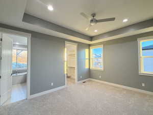 Unfurnished bedroom featuring light carpet, a walk in closet, ensuite bath, ceiling fan, and a closet