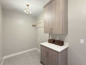 Clothes washing area featuring cabinets, hookup for a washing machine, and an inviting chandelier