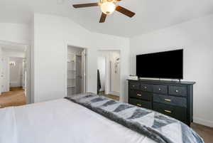 Carpeted bedroom featuring a walk in closet, ceiling fan, a closet, and lofted ceiling