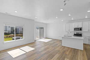 Kitchen featuring light hardwood / wood-style floors, a center island with sink, sink, stainless steel appliances, and white cabinetry