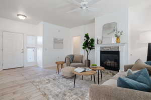 Living room featuring ceiling fan, a stone fireplace, and light wood-type flooring