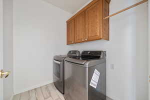 Clothes washing area featuring independent washer and dryer, light hardwood / wood-style floors, and cabinets