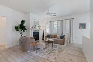 Living room with a tiled fireplace, light wood-type flooring, and ceiling fan