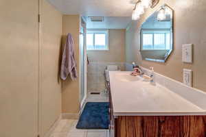 Bathroom featuring vanity, a textured ceiling, tile patterned floors, tile walls, and a shower with door