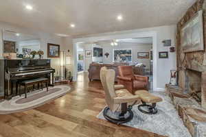 Living room featuring ceiling fan, a stone fireplace, a textured ceiling, and light hardwood / wood-style floors