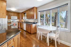 Kitchen with sink, white appliances, a textured ceiling, hardwood / wood-style flooring, and dark stone counters