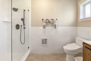 One of two owner's suites. Bathroom with vanity, toilet, heating unit, walk in shower, and tile patterned flooring