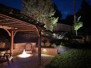 Patio at night with an outdoor fire pit and a pergola