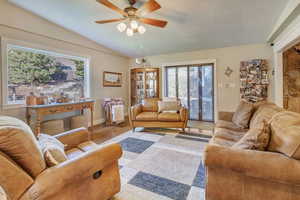 Living room featuring a textured ceiling, vaulted ceiling, light wood-type flooring, and ceiling fan