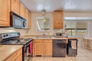 Kitchen featuring black appliances, light tile patterned flooring, sink, and light brown cabinetry