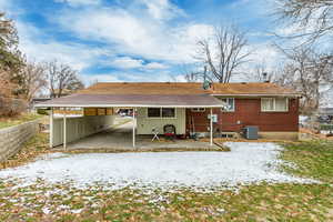 Snow covered back of property with central air condition unit and a carport