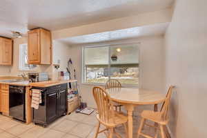 Kitchen with sink, light tile patterned floors, a textured ceiling, black dishwasher, and light brown cabinetry