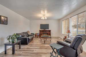 Living room with an inviting chandelier, a textured ceiling, and light wood-type flooring