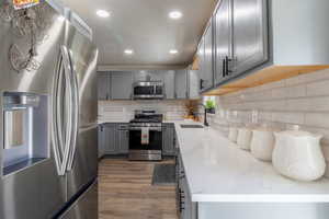 Kitchen featuring light stone counters, sink, gray cabinets, appliances with stainless steel finishes, and dark hardwood / wood-style flooring