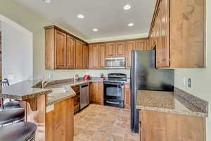 Kitchen featuring a breakfast bar, light stone counters, sink, kitchen peninsula, and black appliances