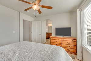 Carpeted bedroom featuring connected bathroom and ceiling fan