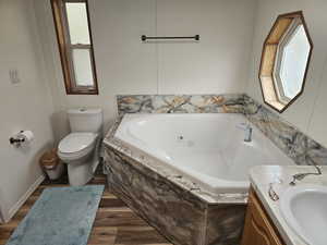 Bathroom featuring hardwood / wood-style floors, a relaxing tiled tub, toilet, and vanity