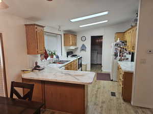 Kitchen with kitchen peninsula, white appliances, vaulted ceiling, washing machine and dryer, and light hardwood / wood-style floors