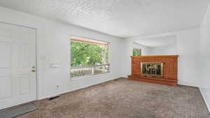 Unfurnished living room with carpet flooring, a fireplace, baseboards, and a textured ceiling