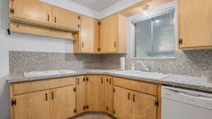 Kitchen with dishwasher, a sink, backsplash, and light countertops