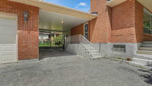Entrance to property featuring an attached carport, brick siding, and asphalt driveway