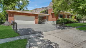 View of front of house with driveway, brick siding, a garage, a mountain view, and a front lawn