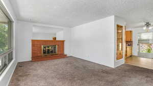 Unfurnished living room featuring carpet, a brick fireplace, ceiling fan, and a textured ceiling