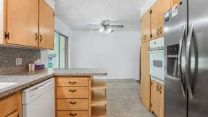 Kitchen with white appliances, decorative backsplash, a ceiling fan, a peninsula, and a textured ceiling