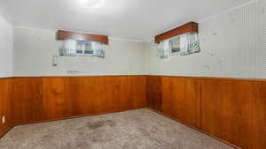 Carpeted empty room featuring ornamental molding, wooden walls, a wainscoted wall, and wallpapered walls