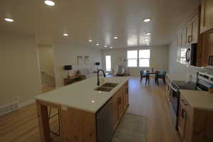 Kitchen with a center island with sink, appliances with stainless steel finishes, light wood-type flooring, and sink