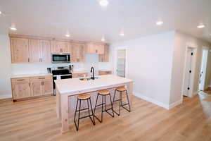 Kitchen with sink, light hardwood / wood-style flooring, a kitchen island with sink, light brown cabinetry, and appliances with stainless steel finishes