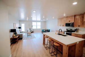 Kitchen with a center island with sink, sink, light hardwood / wood-style floors, a kitchen bar, and stainless steel appliances