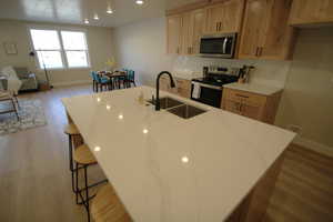 Kitchen featuring light hardwood / wood-style floors, a breakfast bar area, sink, light stone counters, and appliances with stainless steel finishes