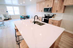 Kitchen featuring a breakfast bar, light brown cabinets, sink, light hardwood / wood-style flooring, and stainless steel appliances