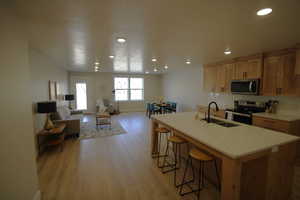 Kitchen featuring light hardwood / wood-style flooring, a breakfast bar, sink, an island with sink, and appliances with stainless steel finishes