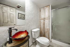 Full bath featuring a textured wall, a shower stall, toilet, and a textured ceiling