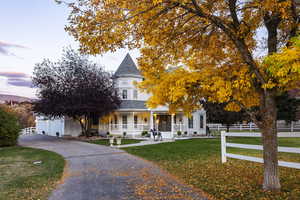 Victorian house featuring covered porch, fence, roof with shingles, and a front lawn