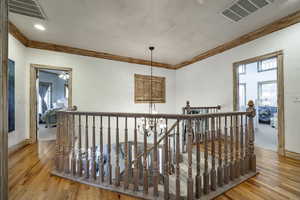 Hall featuring wood-type flooring, visible vents, ornamental molding, and an upstairs landing