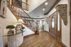 Foyer with stairs, a textured wall, ornamental molding, and wood finished floors