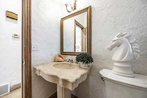 Bathroom with visible vents, wood finished floors, a sink, toilet, and a textured wall