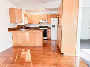 Kitchen with vaulted ceiling, kitchen peninsula, sink, light brown cabinetry, and white appliances