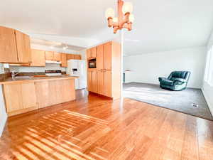 Kitchen with kitchen peninsula, stove, sink, white refrigerator with ice dispenser, and light brown cabinetry