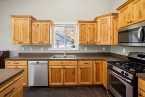 Kitchen featuring dark tile patterned floors. Kitchen with oven, stove, washer, sink, and refrigerator/freezer. Appliances with stainless steel finishes.